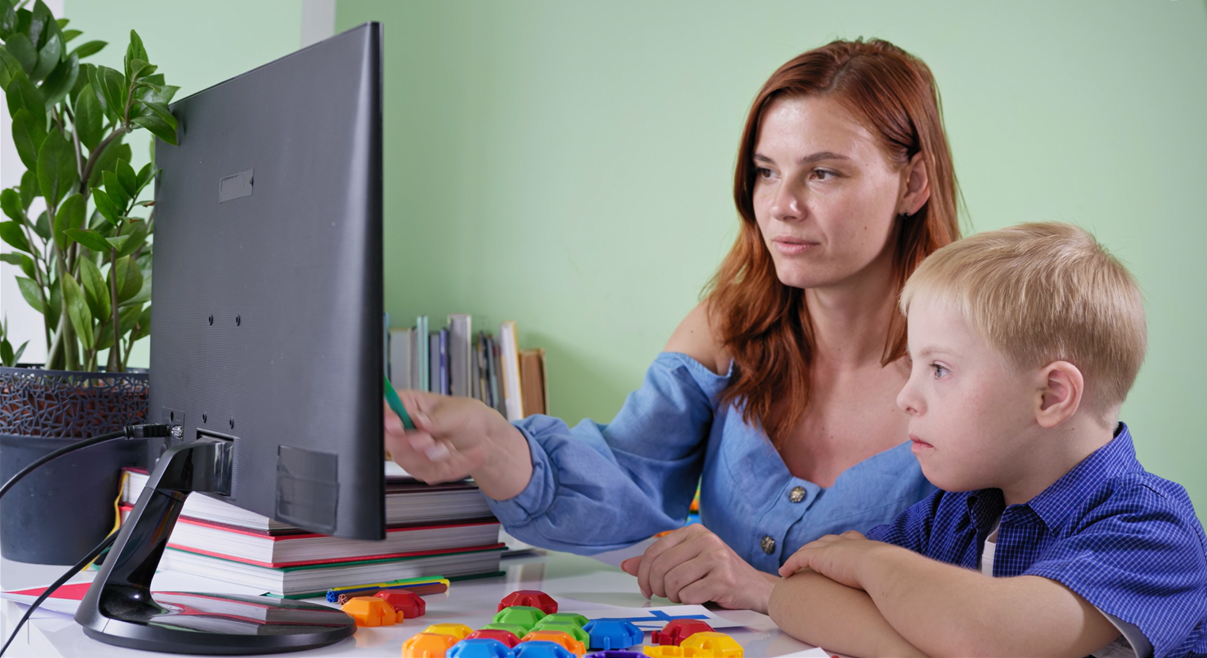 Consejera escolar sentada junto a un niño con necesidades especiales, ambos mirando a la pantalla de una computadora.