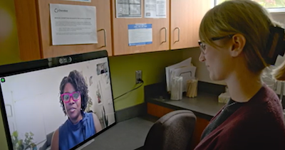 Doctora visible en la pantalla de una computadora, realizando una teleconsulta con una paciente que se encuentra en una clínica.