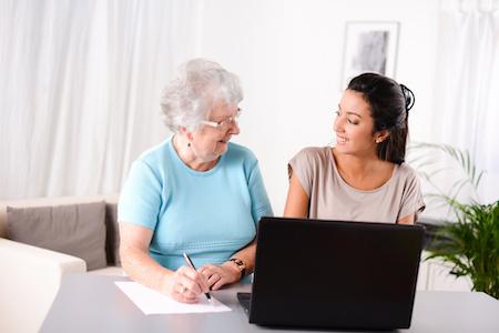Young woman teaching older adult how to use computer.