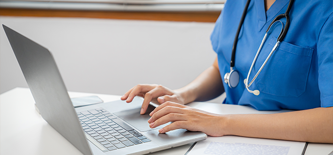 Upclose image of health care provider with stethoscope typing on a laptop.